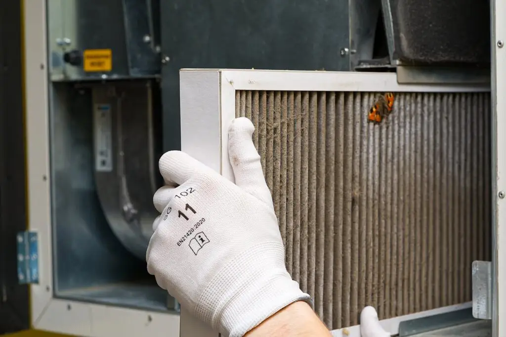 A person wearing white gloves installing or replacing an air filter in a heating, ventilation, and air conditioning (HVAC) system.