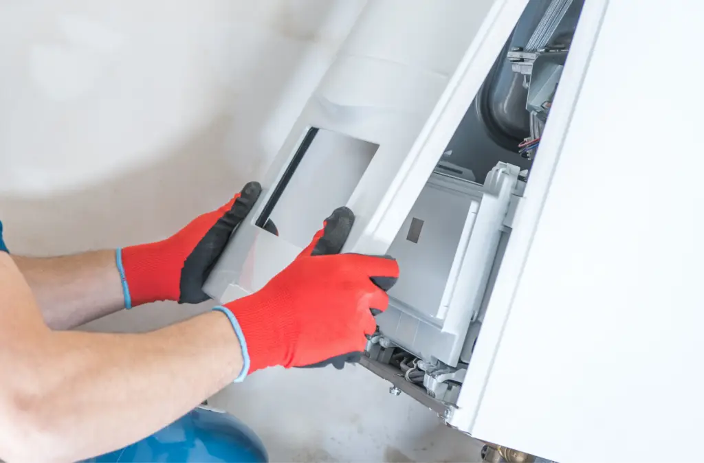 Person wearing red gloves installing or repairing the internal panel of a dishwasher or washing machine.