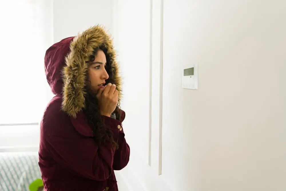 Woman in front of thermostat because heat pump is not heating.